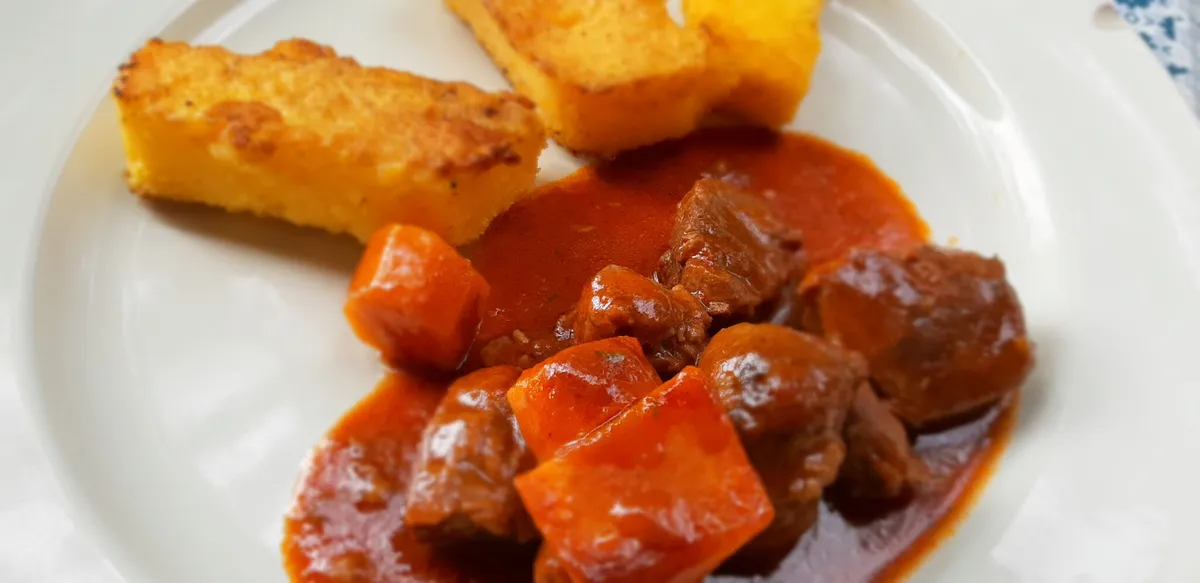 Une assiette rustique avec une joue de porc braisée nappée d'une sauce brune, pommes vapeur et persil frais