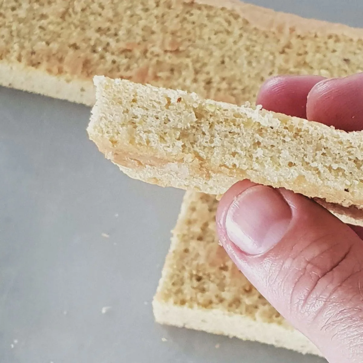 Gros plan sur un pain de Gênes doré posé sur une planche en bois, amandes effilées et poudre d'amande visibles