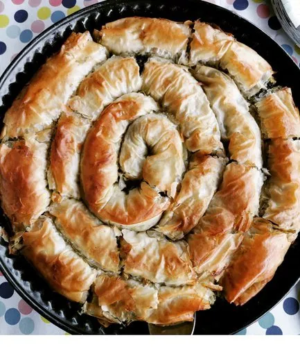 Feuilletés dorés posés sur une planche en bois, feuilles de pâte filo superposées et beurre fondu à côté