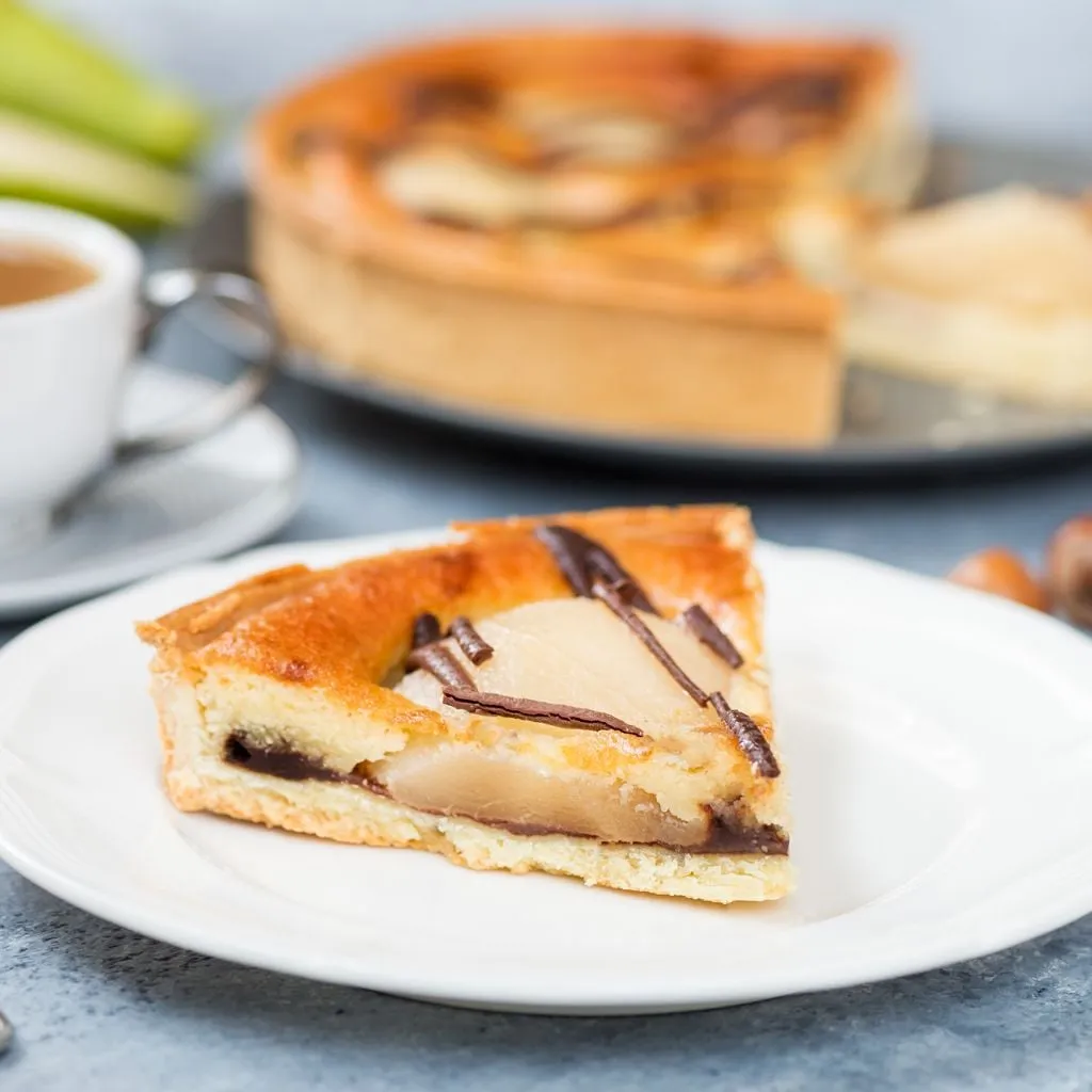 Tarte ronde sur une assiette en faïence ; nappage brillant chocolat, tranches de poire disposées en éventail, une fourchette à côté